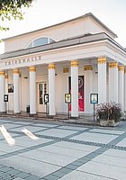 historisches Gebaeude auf einem großen gepflasterten Platz, Parkbaenke stehen vor dem Gebaeude